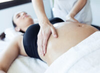 Two hands massaging a pregnant woman's belly